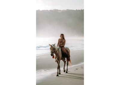 Frau reitet mit Pferd am Strand entlang